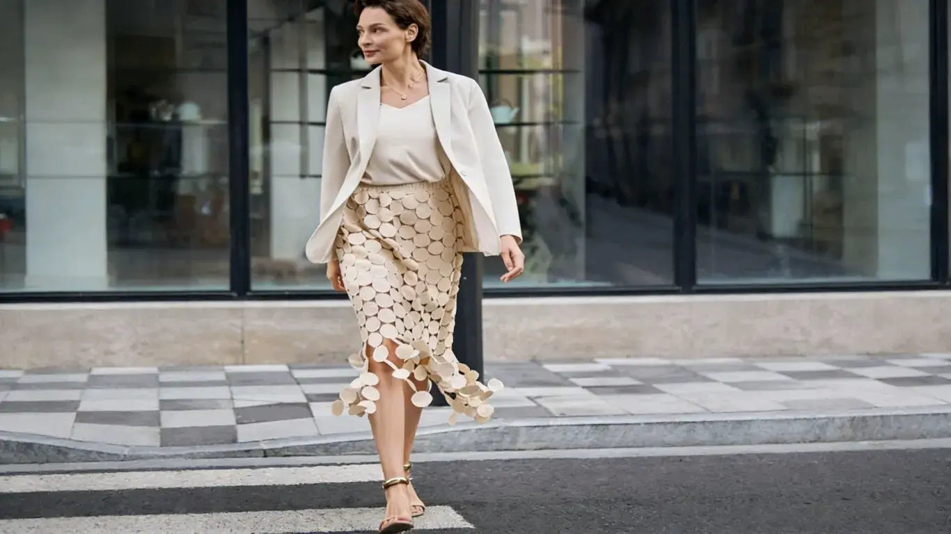 Blonde woman in white lace camisole & gold disc midi skirt with white woven clutch
