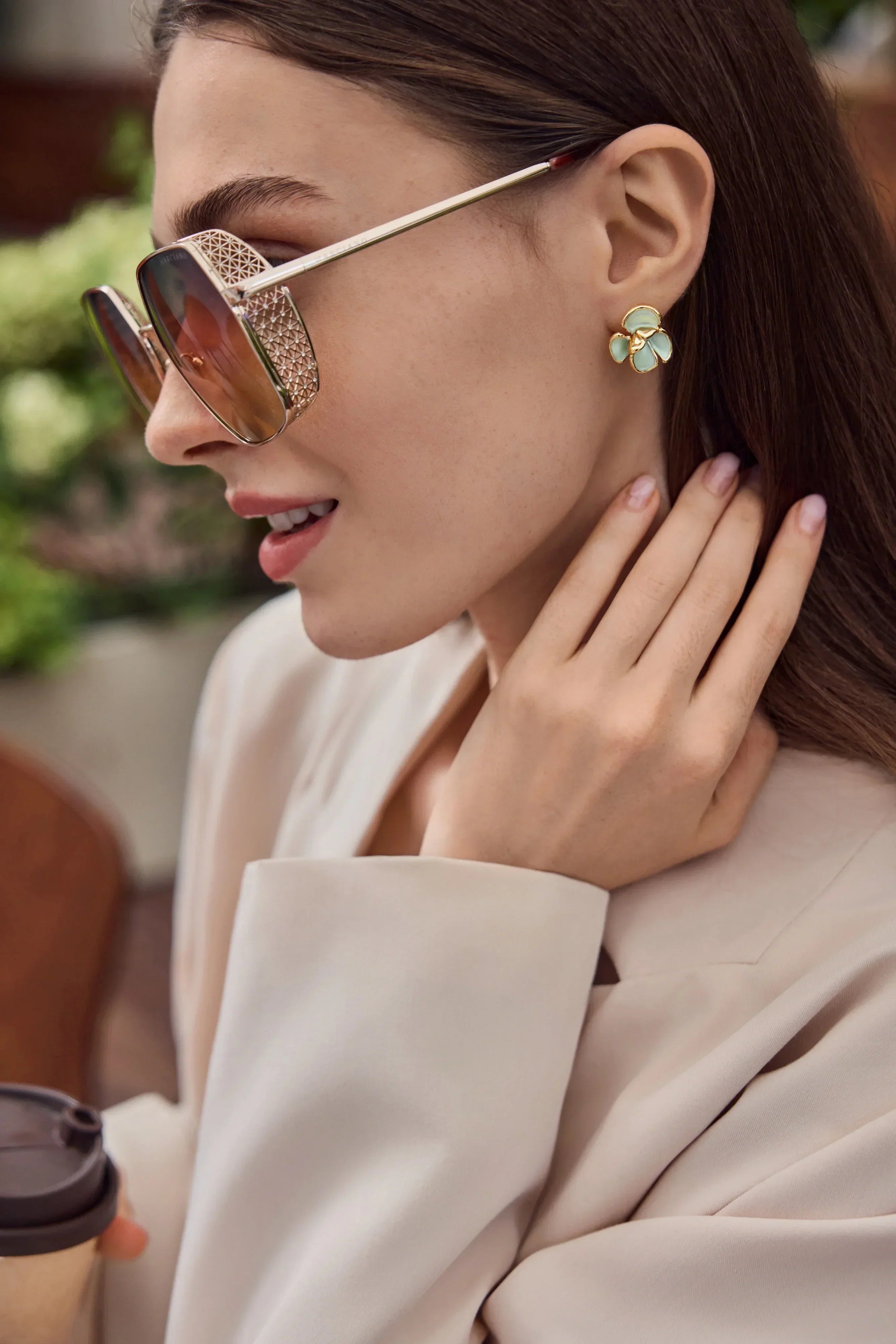 Professional woman wearing a beige blazer and Cicy Bell gold floral stud earrings holding a coffee cup
