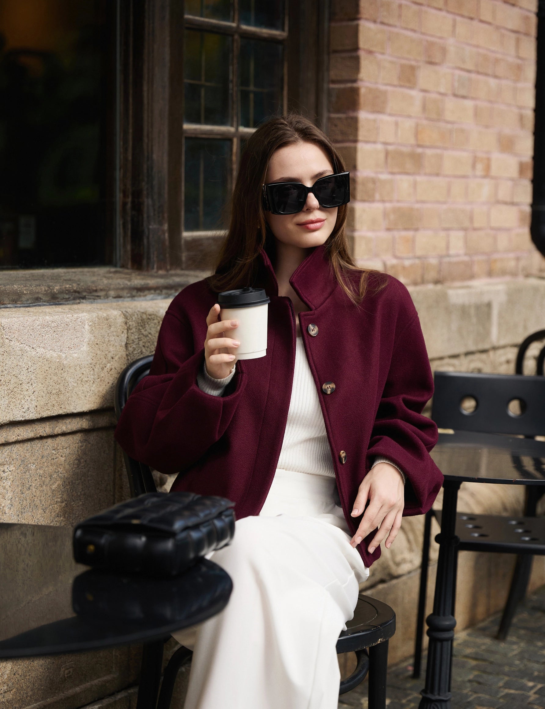 Elegant woman in a chic burgundy winter cropped coat having coffee outside, styling an old money aesthetic look