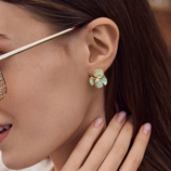 Woman with elegant smart casual workwear putting on 14k gold plated light green flower stud earrings