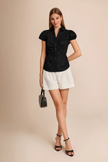 Summer 2026 outfit idea featuring a black short sleeve blouse paired with tailored white high-waisted shorts