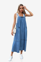 A modern boho-chic Cicy Bell denim maxi dress with a multi-tiered silhouette and shabby-chic fringe accents. Highlights the adjustable metal buckles and oversized aesthetic, perfect for layering over tees or sweaters for farmers' market runs or casual coffee dates.