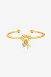 Cicy Bell Women's 18k Gold Plated Initial Bangle featuring a symbolic love knot design and a sparkling CZ heart charm. This personalized open-cuff bracelet offers an adjustable $60\text{mm}$ fit for bridesmaids or best friends.