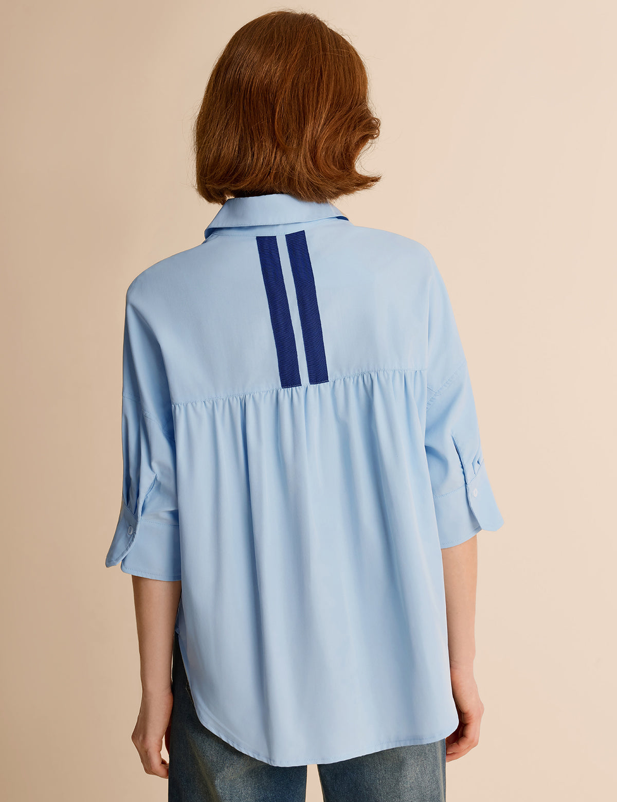 Back view of a sky blue oversized women's shirt featuring a slimming dark navy vertical contrast stripe
