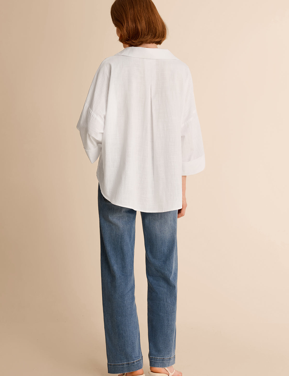 Back view of a relaxed fit white high-low hem button-down shirt for women