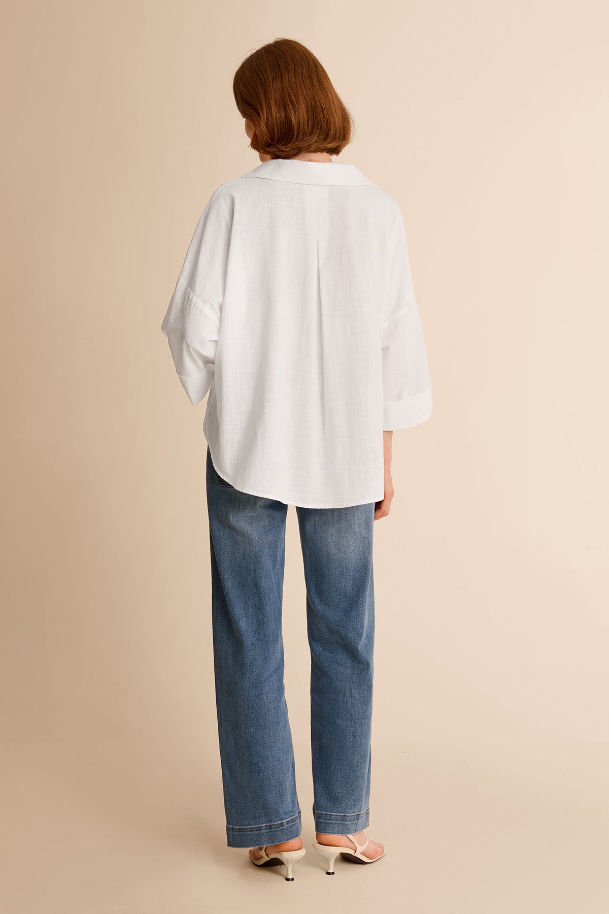 Back view of a relaxed fit white high-low hem button-down shirt for women