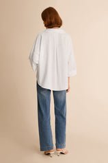 Back view of a relaxed fit white high-low hem button-down shirt for women
